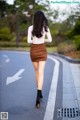 A woman walking down the street in a brown skirt.