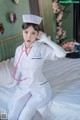 A woman in a white nurse outfit sitting on a bed.