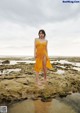 A woman in a yellow dress standing on a rocky beach.