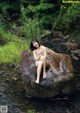 A woman sitting on a rock in the middle of a stream.