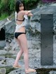 A woman in a black bikini standing on a rock by the water.